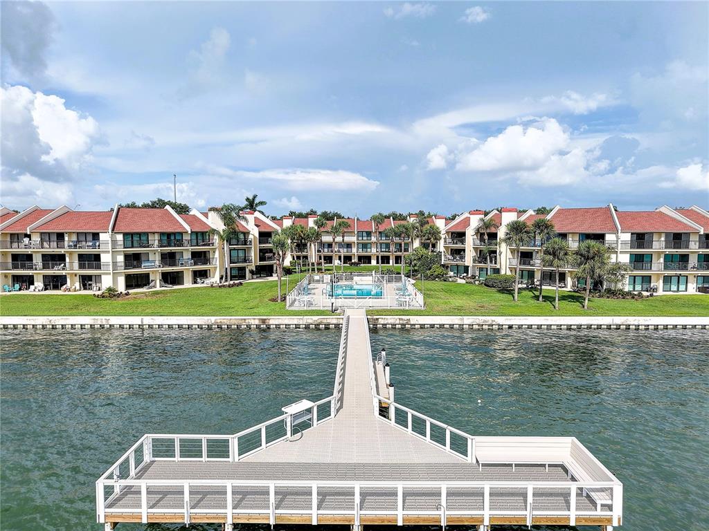 An aerial view shows a long wooden pier extending into water toward a multi-story apartment complex — 7510 SUNSHINE SKYWAY LANE S UNIT T13, ST PETERSBURG, FL