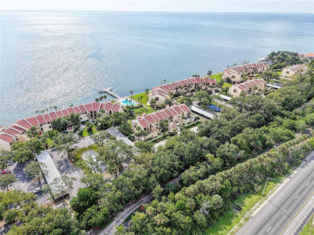 An aerial view shows a waterfront condominium complex with red roofs, pools, and parking areas — 7510 SUNSHINE SKYWAY LANE S UNIT T13, ST PETERSBURG, FL
