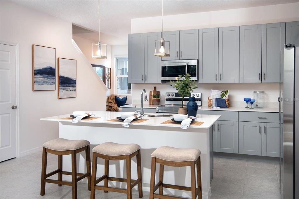 A kitchen features a white island with three stools, gray cabinets, and stainless steel appliances — 1536 SILVER LINING WAY, APOPKA, FL