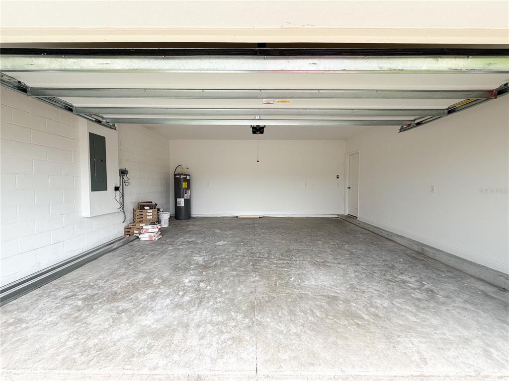 An empty two-car garage with a concrete floor, white walls, and a water heater — 4152 SAGEFIELD DR, HARMONY, FL