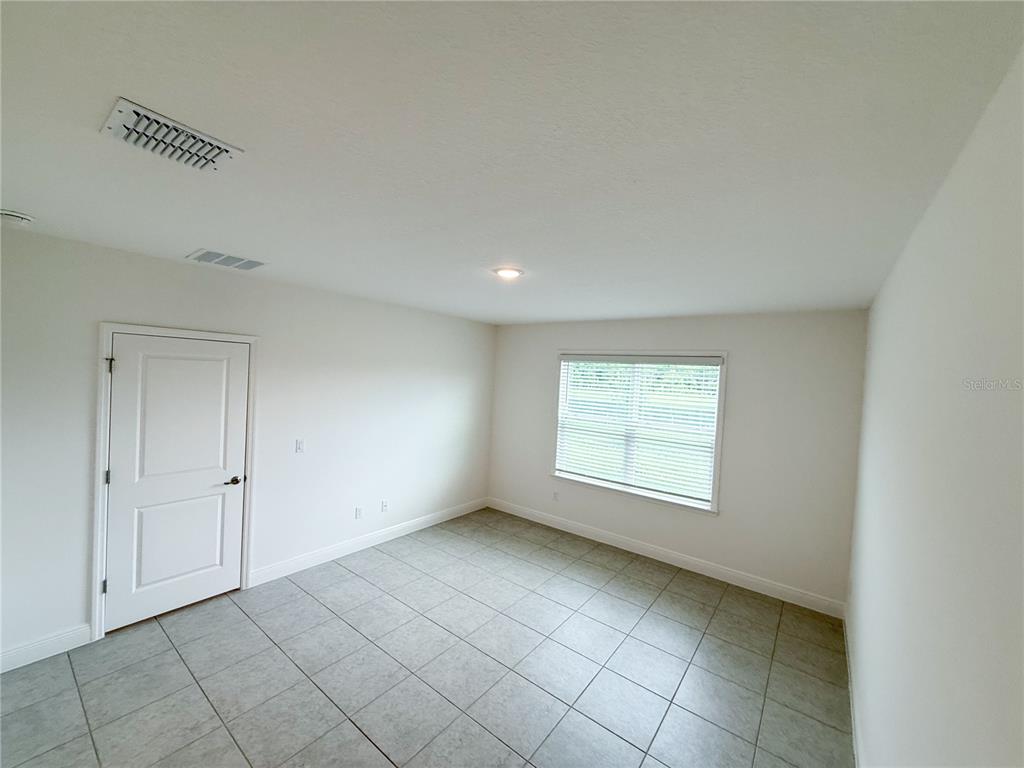 An empty room features light-colored walls, a single window with blinds, and gray tiled flooring — 4152 SAGEFIELD DR, HARMONY, FL