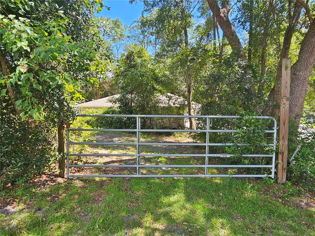 A metal farm gate stands in front of a wooded area and a house — 18TH STREET, ORANGE CITY, FL