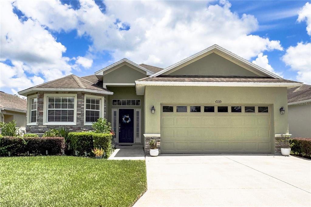 A single-story house with a green stucco exterior, stone accents, and a two-car garage — 6335 SILVER LEAF LANE, LAKELAND, FL