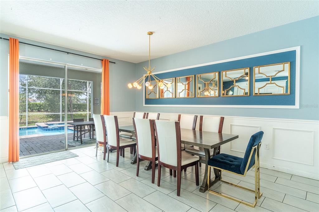 A dining room with a long table, white chairs, blue walls, and a pool view — 1532 MAIDSTONE COURT, DAVENPORT, FL