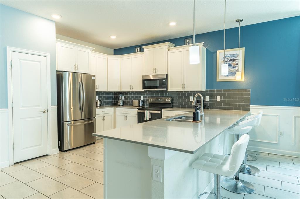 A kitchen features white cabinets, stainless steel appliances, a gray tile backsplash, and a breakfast bar — 1532 MAIDSTONE COURT, DAVENPORT, FL