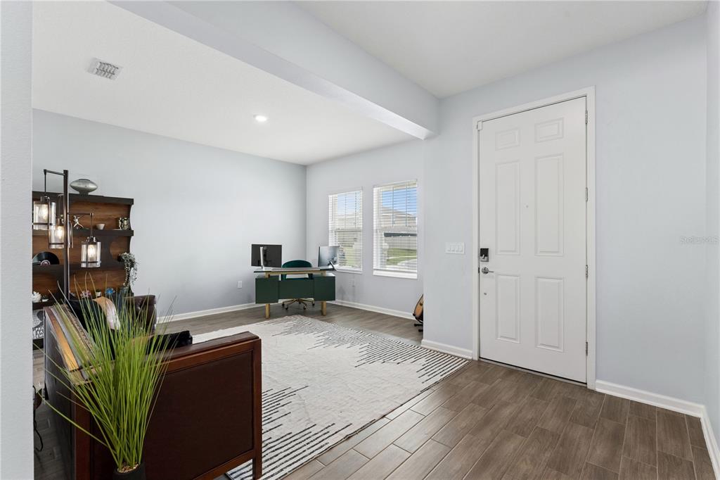 A home office with light blue walls, wood-look tile flooring, and a white entry door — 1855 BLACK MAPLE PLACE, OCOEE, FL