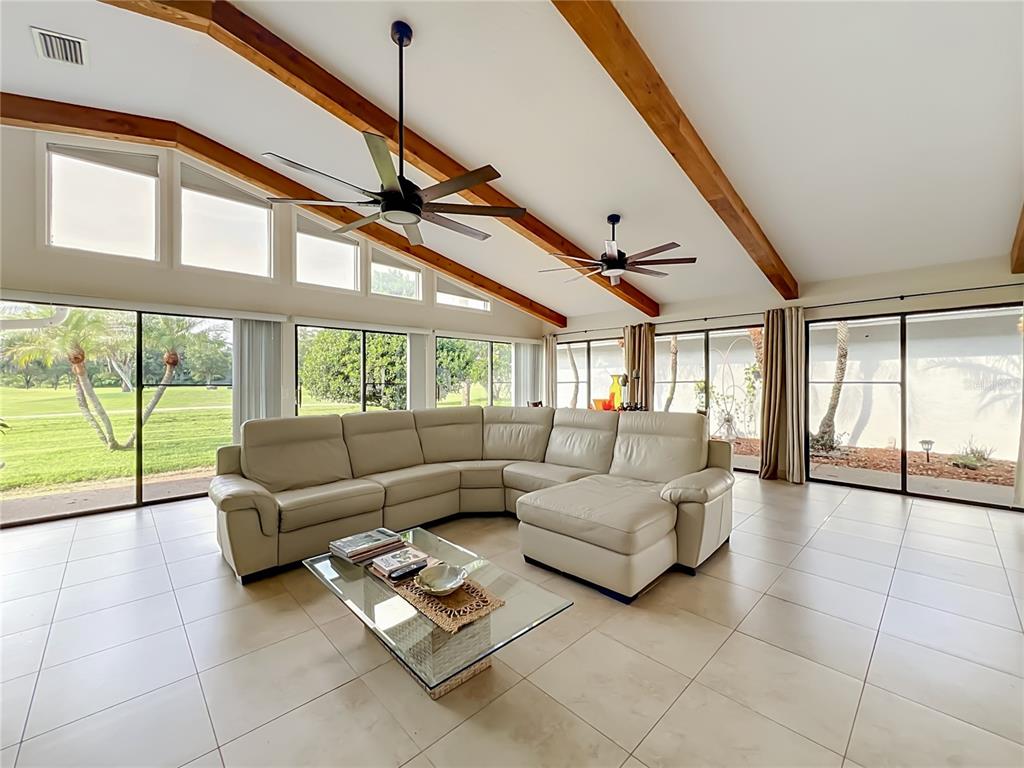A living room features a large sectional sofa, vaulted ceilings with wood beams, and floor-to-ceiling windows — 6328 GREENGATE DRIVE, ORLANDO, FL