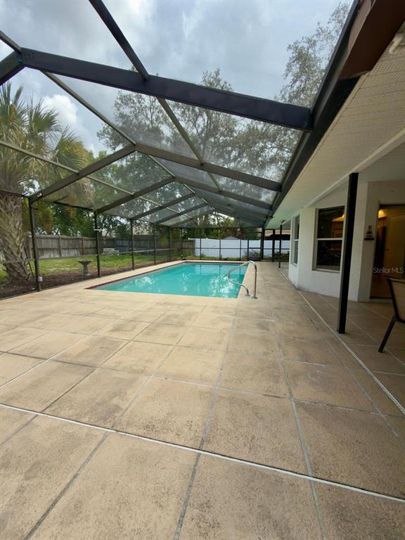A screened-in patio features a rectangular swimming pool and light-colored concrete pavers — 13322 JAY COURT, SPRING HILL, FL