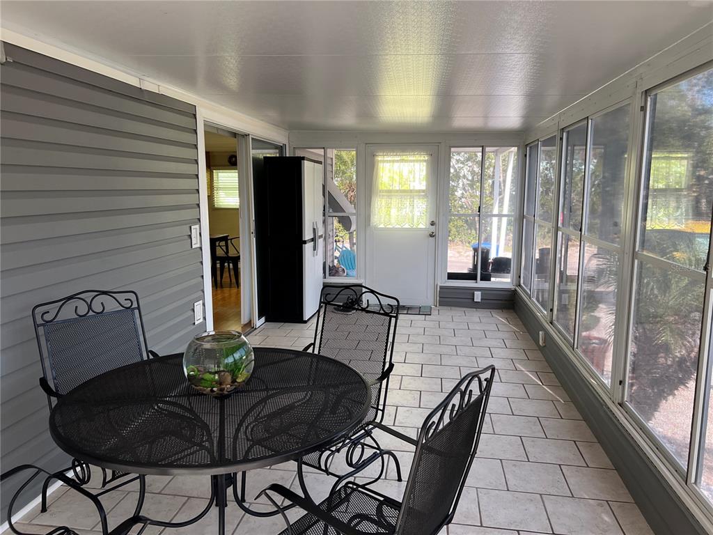 A sunroom features tile flooring, a metal dining set, and large windows overlooking the outdoors — 2601 GULF DRIVE N UNIT S2, BRADENTON BEACH, FL