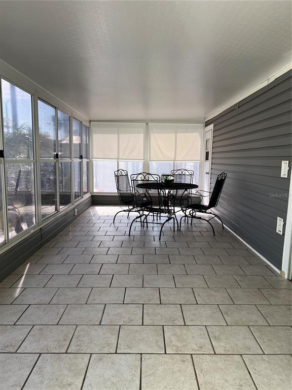 A sunroom features tiled flooring, a dark gray paneled wall, and a metal dining set — 2601 GULF DRIVE N UNIT S2, BRADENTON BEACH, FL