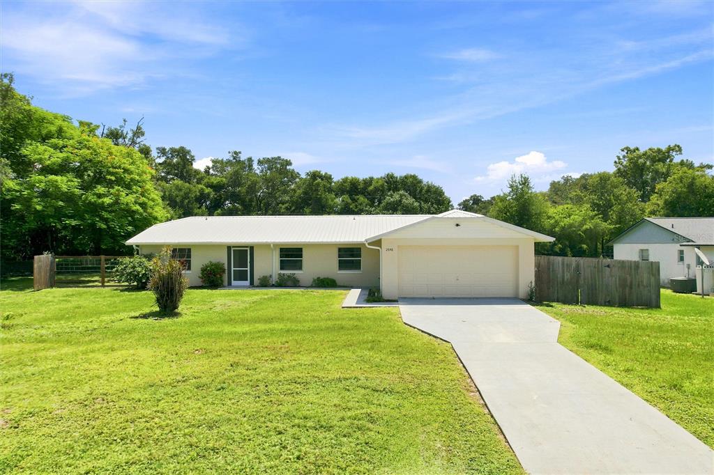 A single-story house with a white metal roof, beige siding, and an attached two-car garage — 2848 SE NORMAN AVENUE, ARCADIA, FL