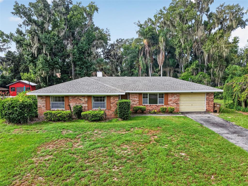 A single-story brick house with a shingled roof and an attached garage sits on grass — 8050 SPRING DRIVE, YALAHA, FL