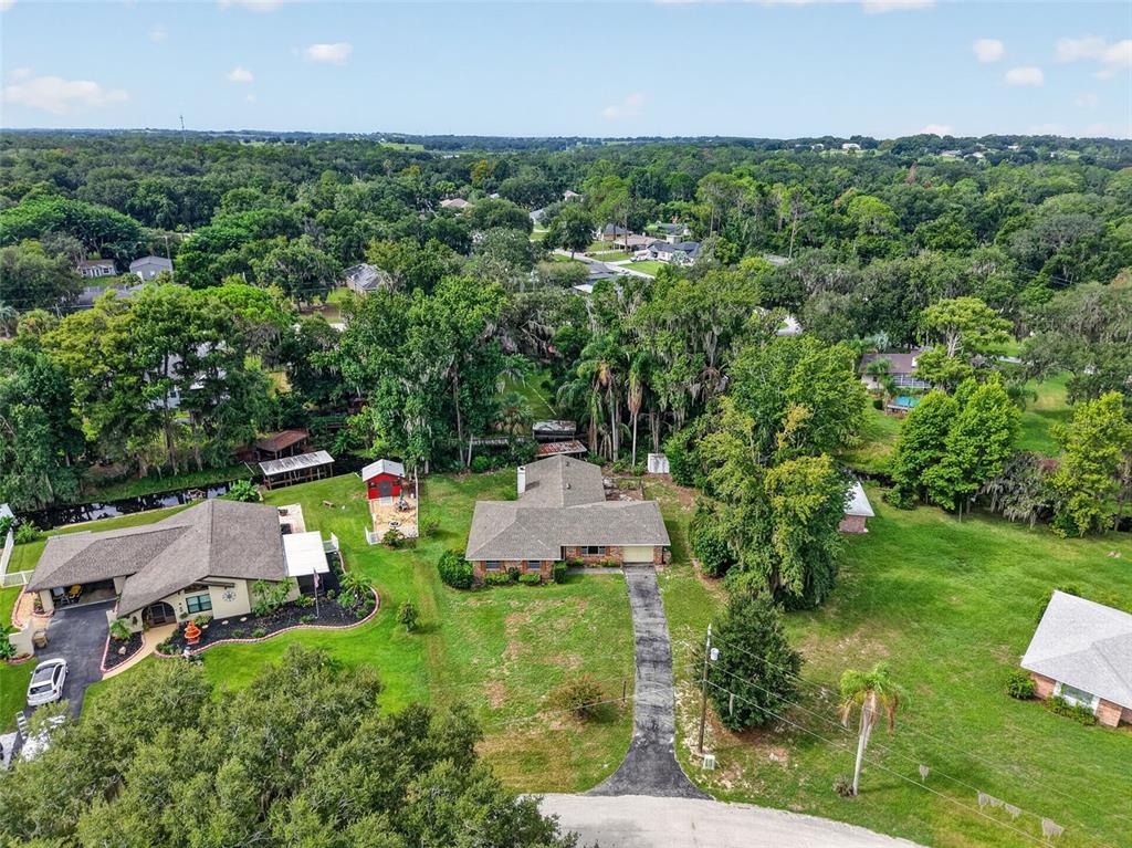 An aerial view shows two houses with driveways, a red shed, and trees on a grassy lot — 8050 SPRING DRIVE, YALAHA, FL