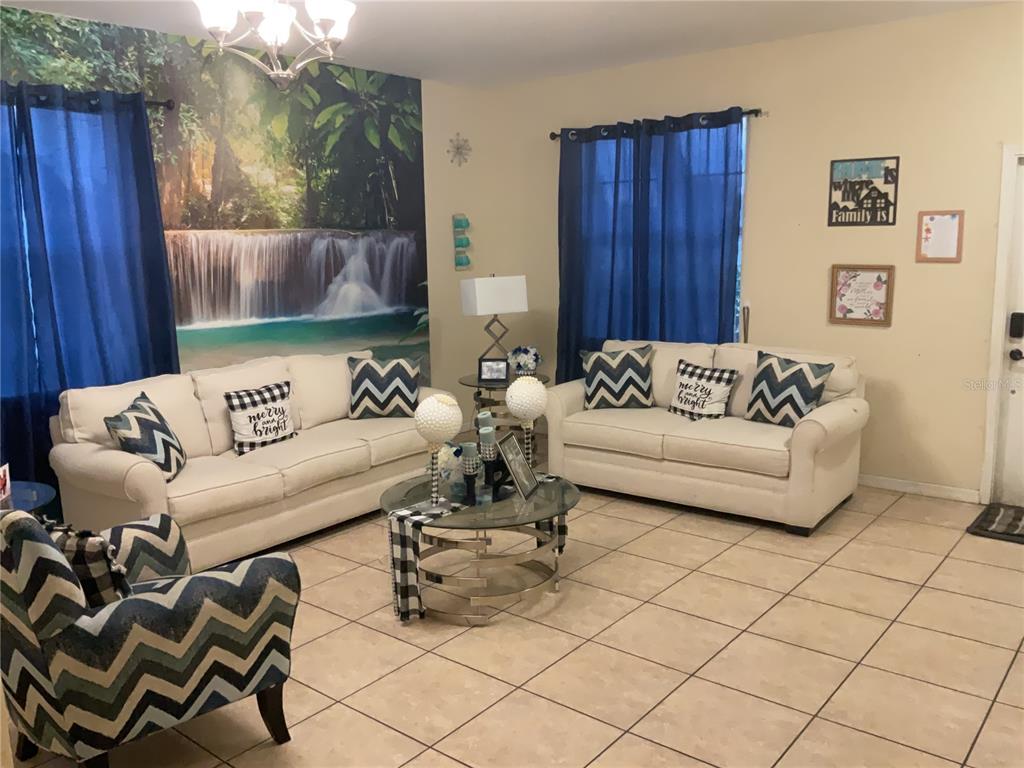 A living room features two cream sofas, a glass coffee table, and a waterfall mural — 11007 STANDING STONE DRIVE, WIMAUMA, FL
