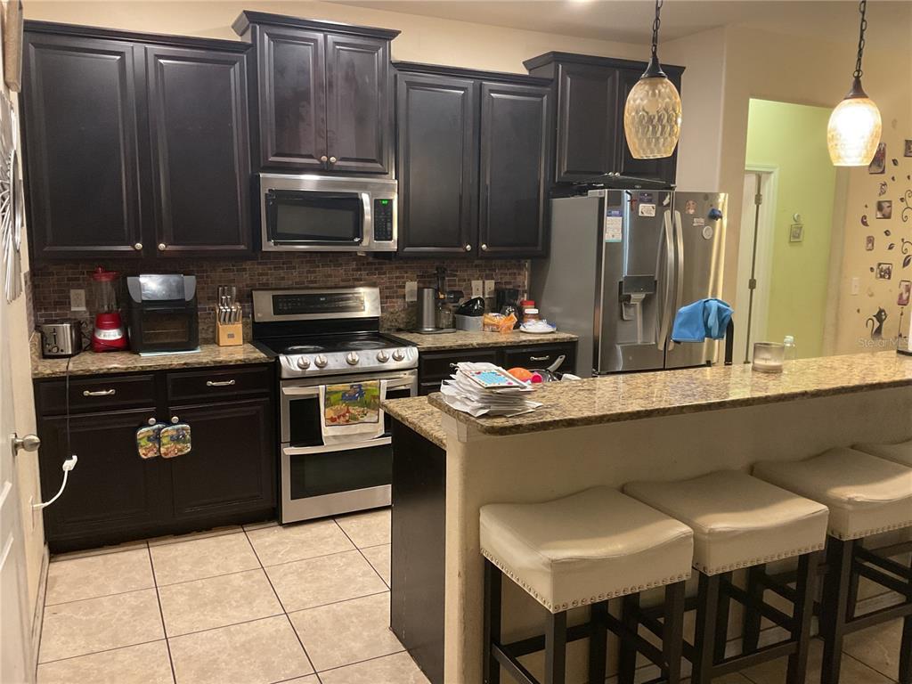 A kitchen features dark wood cabinets, stainless steel appliances, granite countertops, and a breakfast bar — 11007 STANDING STONE DRIVE, WIMAUMA, FL