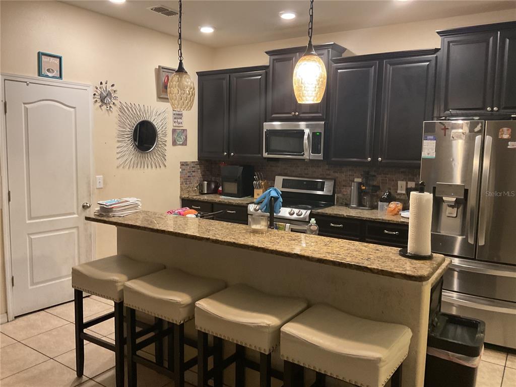 A kitchen features dark wood cabinets, granite countertops, a breakfast bar with stools, and stainless appliances — 11007 STANDING STONE DRIVE, WIMAUMA, FL