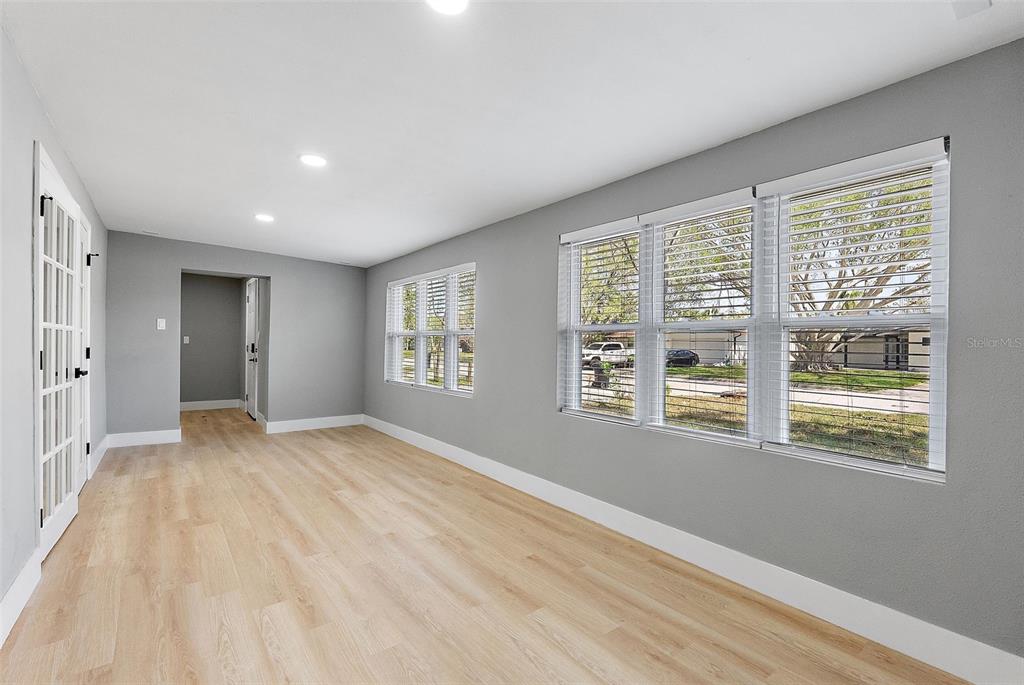 A bright room with gray walls, light wood-look flooring, and large windows with white blinds — 3926 HELENA STREET NE, ST PETERSBURG, FL