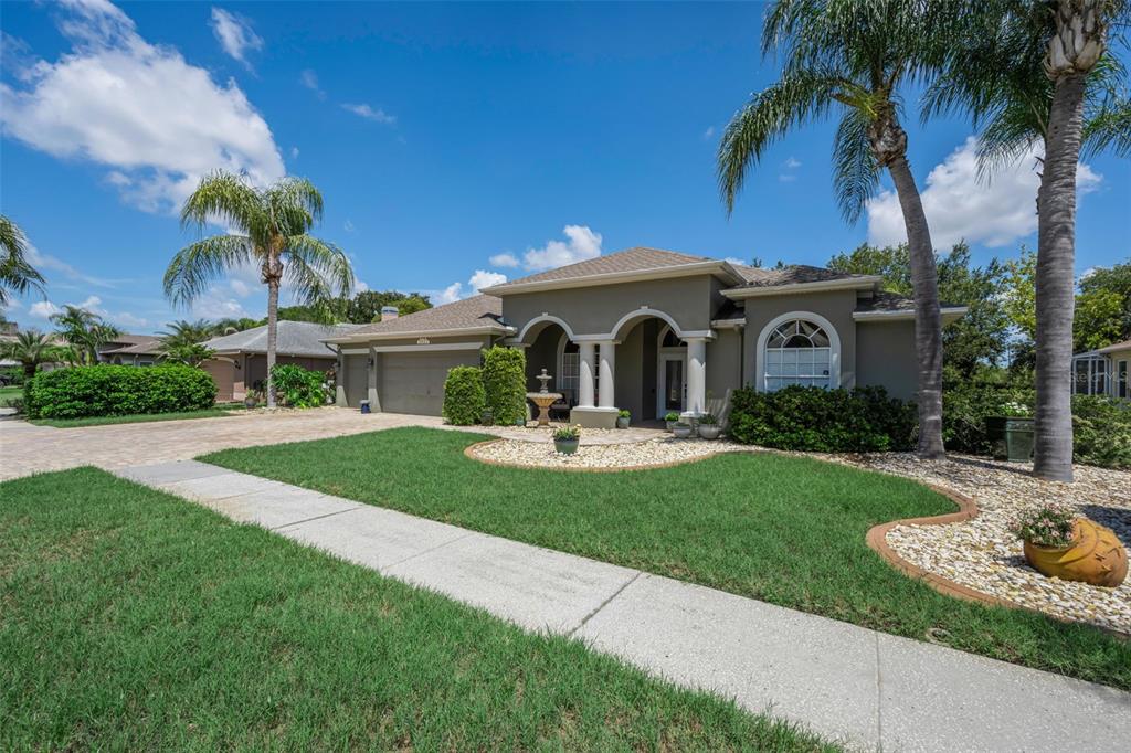 A single-story house with a tan stucco exterior, arched entryway, and a paved driveway — 8843 BEL MEADOW WAY, TRINITY, FL