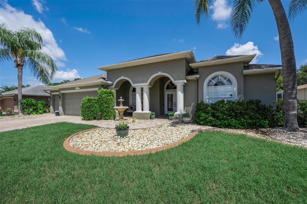 A single-story house with a gray exterior, arched entryway, and a landscaped front yard — 8843 BEL MEADOW WAY, TRINITY, FL