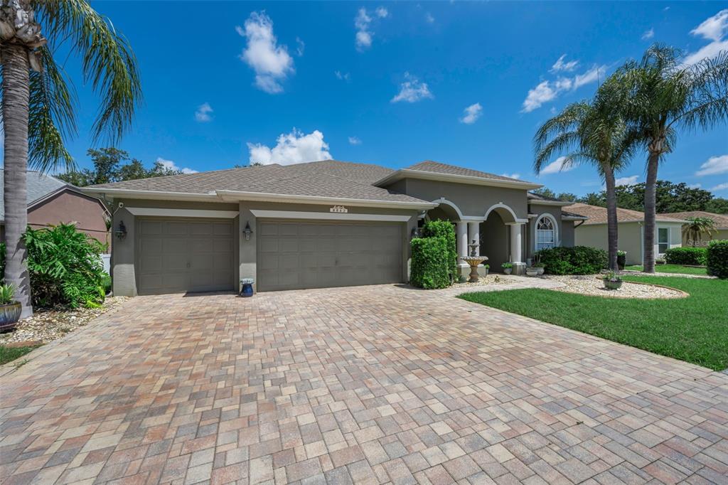 A single-story house with a paved driveway, three-car garage, and palm trees under a blue sky — 8843 BEL MEADOW WAY, TRINITY, FL