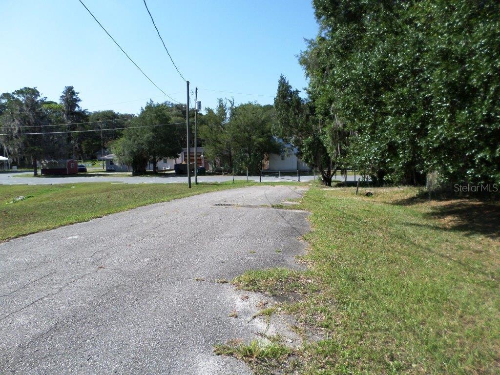 A paved driveway leads toward a road with trees and houses in the background — 00 BLUE HERON CT, DUNNELLON, FL