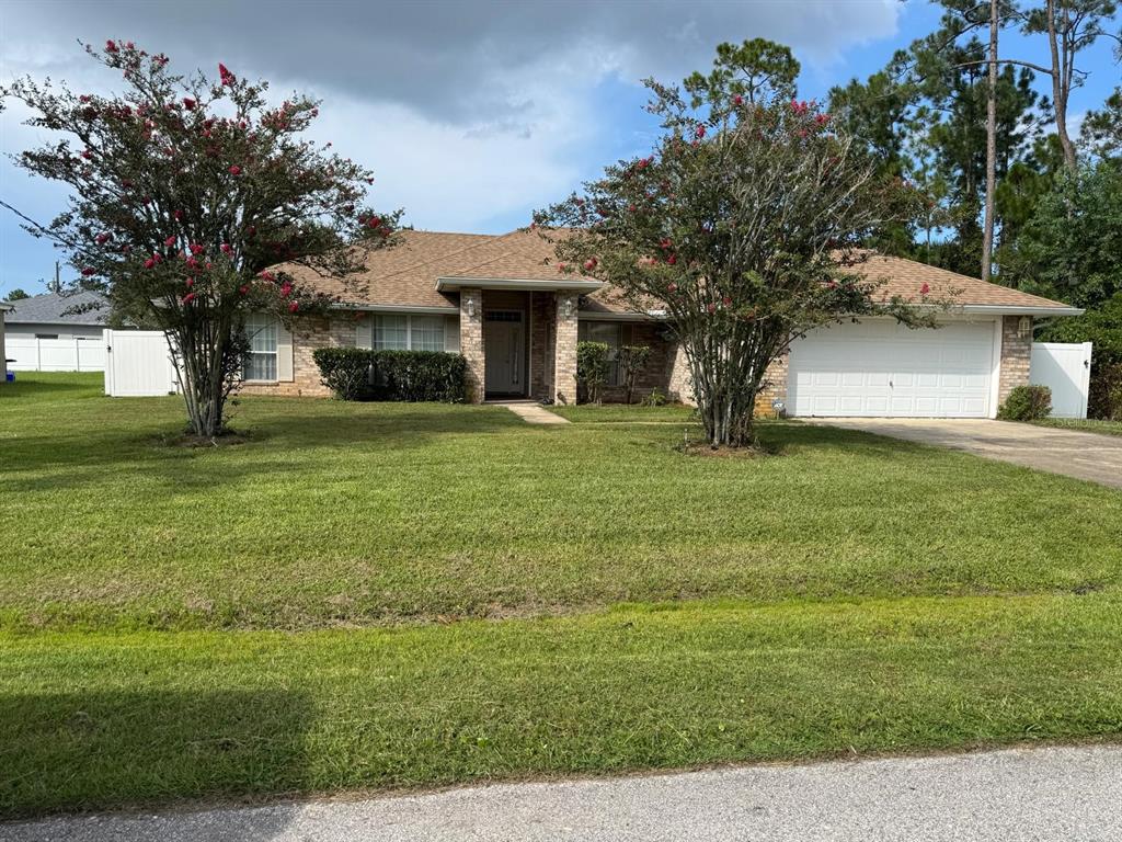 A single-story brick house with a two-car garage and two flowering trees in the yard — 16 RED BARN DRIVE, PALM COAST, FL
