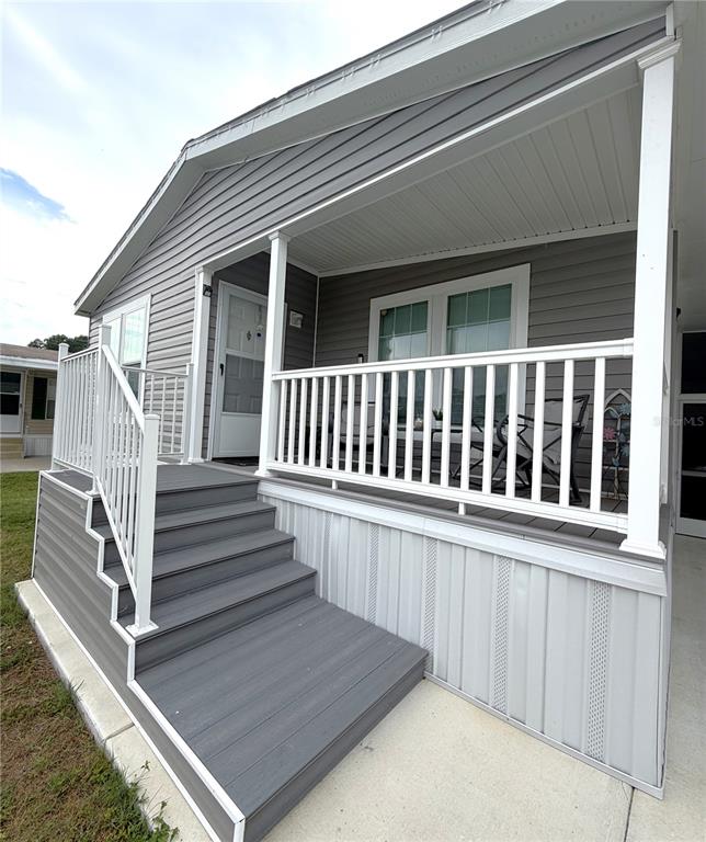 A gray mobile home features a raised front porch with white railings and stairs — 118 JANA CIRCLE, AUBURNDALE, FL