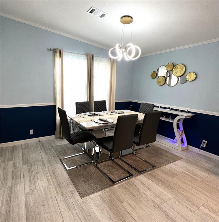 A dining room features a modern chandelier, dark blue wainscoting, and a glass-topped table — 118 JANA CIRCLE, AUBURNDALE, FL