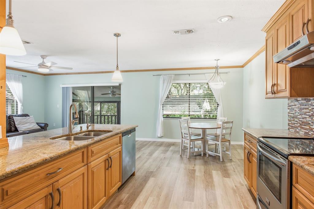 An open-concept kitchen and living area features light wood flooring, a granite island, and cabinetry — 511 MISTLETOE COURT UNIT C, SAFETY HARBOR, FL