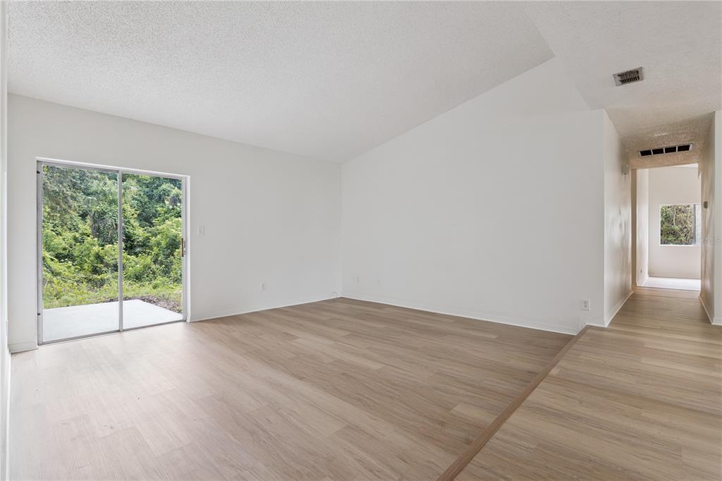 An empty living room with light wood-look flooring, white walls, and a sliding glass door — 110 HOLDERNESS DRIVE, LONGWOOD, FL