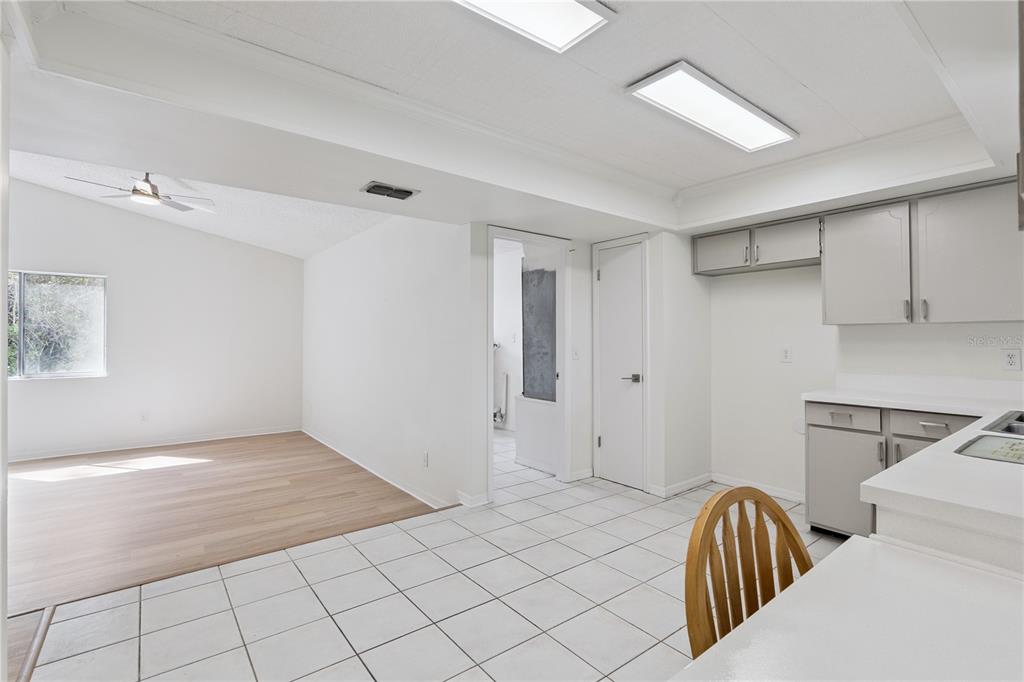 A kitchen with white tile floors and grey cabinets opens into a light-floored living area — 110 HOLDERNESS DRIVE, LONGWOOD, FL