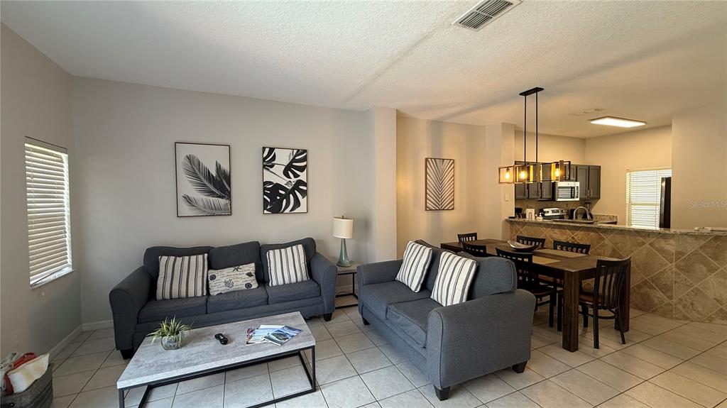 A living room with two gray sofas and a dining area with a kitchen counter — 8517 BAY LILLY LOOP, KISSIMMEE, FL