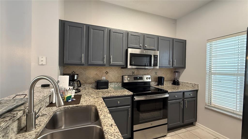 A kitchen features gray cabinets, granite countertops, stainless steel appliances, and a double-basin sink — 8517 BAY LILLY LOOP, KISSIMMEE, FL