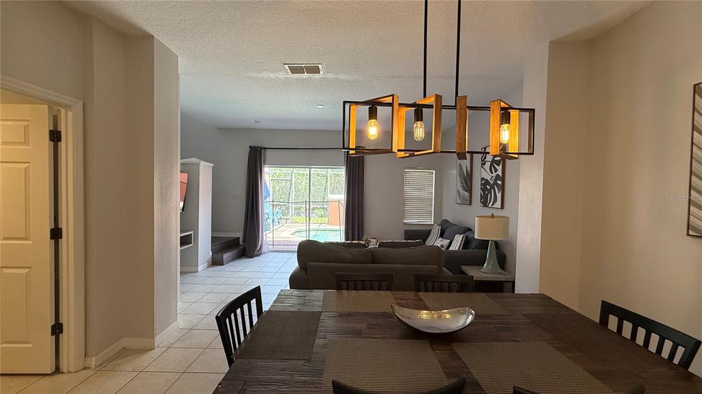A dining area with a wooden table and chandelier overlooks a living room and pool — 8517 BAY LILLY LOOP, KISSIMMEE, FL