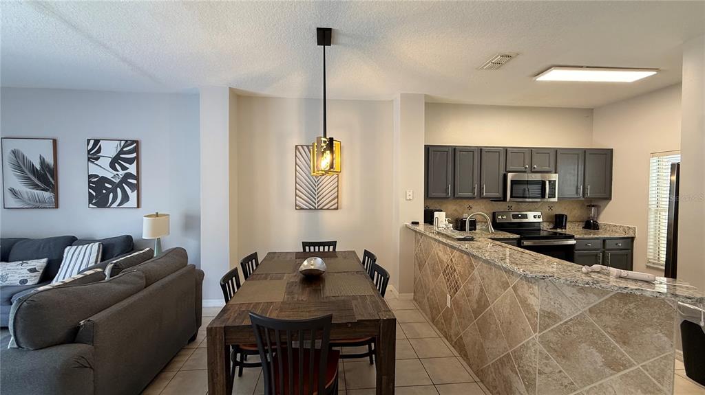 A dining area with a wooden table sits adjacent to a kitchen with granite countertops — 8517 BAY LILLY LOOP, KISSIMMEE, FL