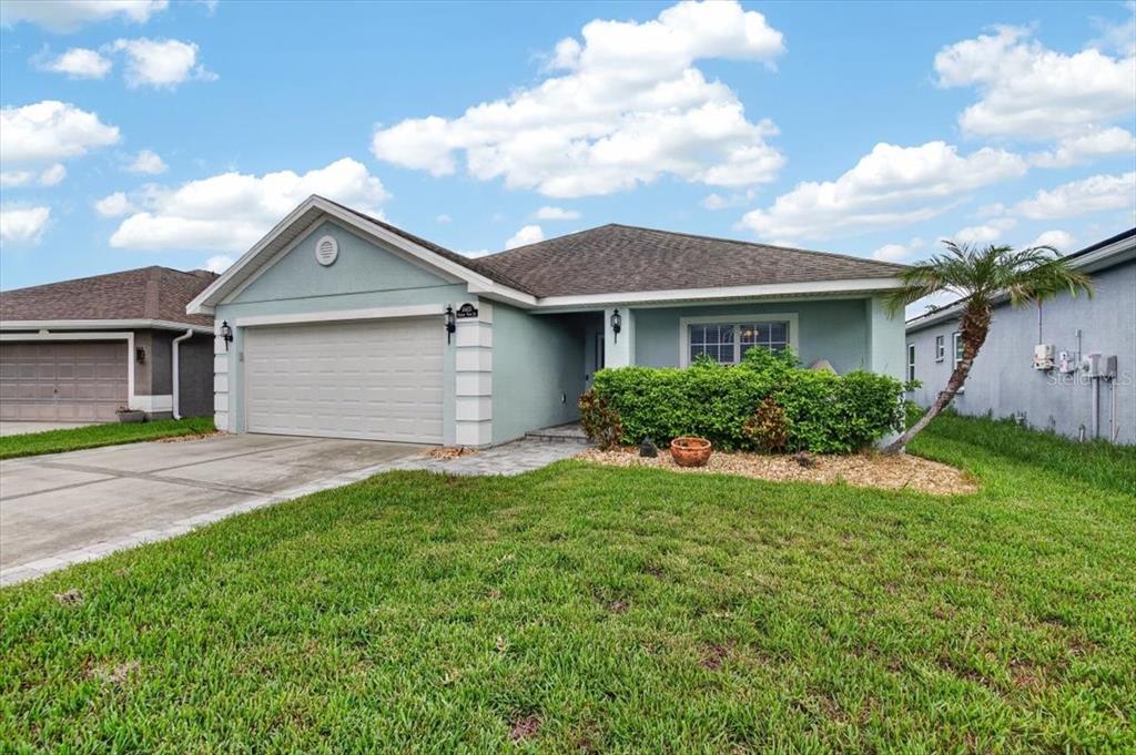 A light blue single-story house with a two-car garage and a front lawn — 14415 BARLEY FIELD DRIVE, WIMAUMA, FL