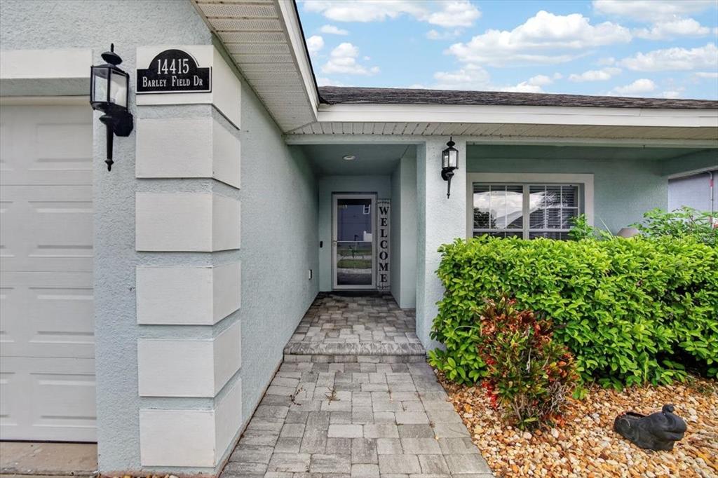 The exterior view shows a light blue house with a paved walkway and front entrance — 14415 BARLEY FIELD DRIVE, WIMAUMA, FL