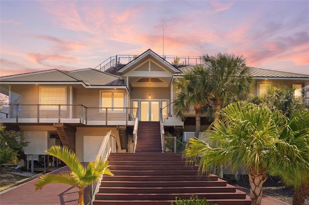 A raised coastal home features a wide wooden staircase leading to a central front entrance — 211 KINGFISHER DRIVE, CAPTIVA, FL