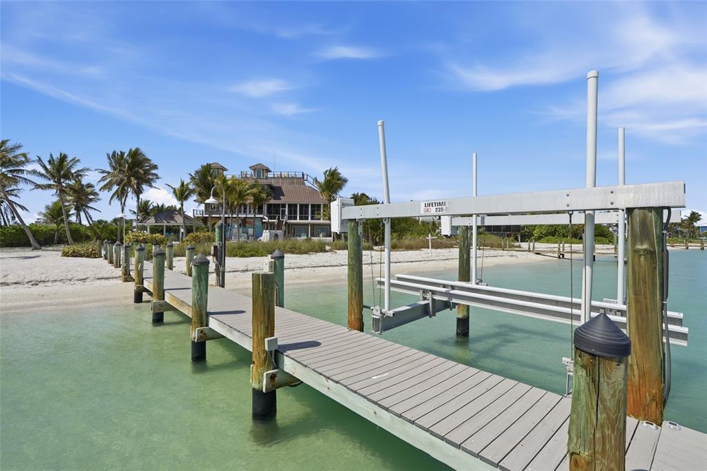 A wooden dock with a boat lift extends into clear water toward a beach house — 211 KINGFISHER DRIVE, CAPTIVA, FL
