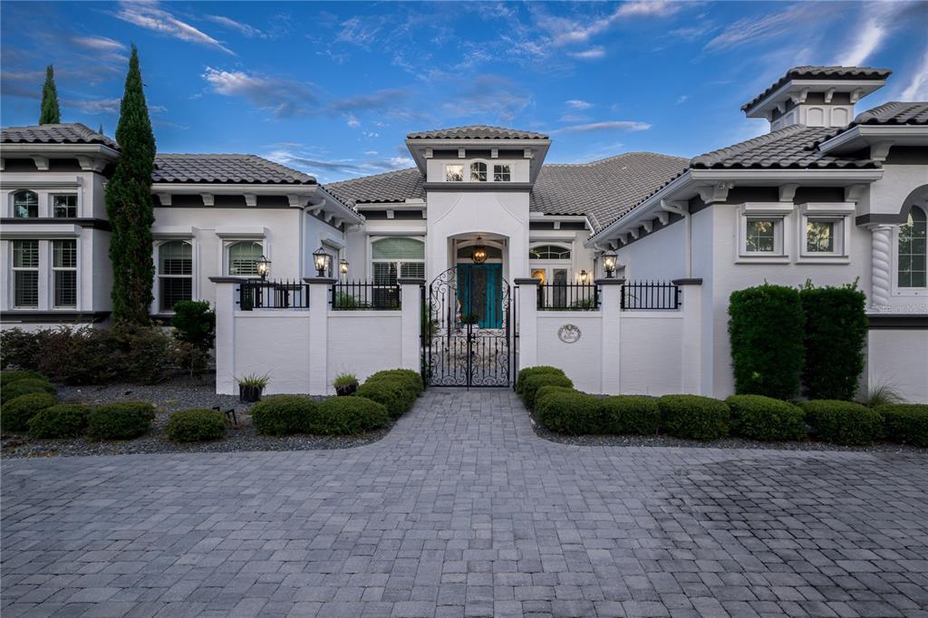 A white stucco house with a tiled roof features a gated courtyard and stone driveway — 1025 SUDBURY LANE, ORMOND BEACH, FL
