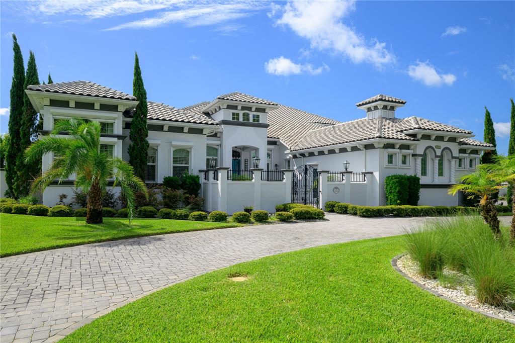 A large, single-story Mediterranean-style house with a paved driveway, palm trees, and a gated courtyard — 1025 SUDBURY LANE, ORMOND BEACH, FL
