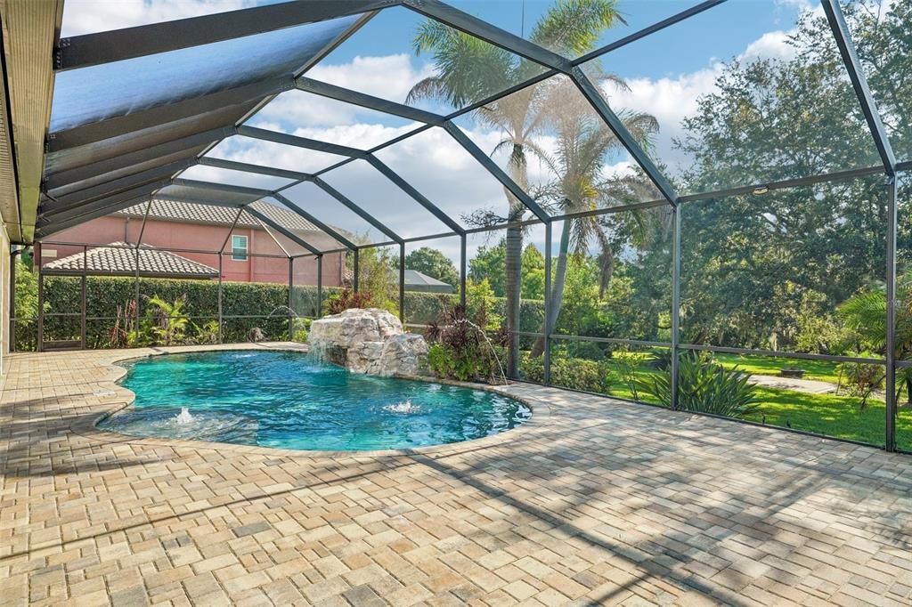A swimming pool with a rock waterfall feature is enclosed by a screened-in patio area — 19711 WELLINGTON MANOR BOULEVARD, LUTZ, FL