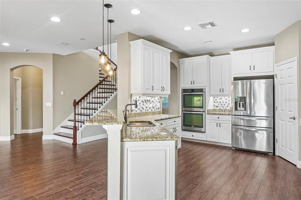 A kitchen with white cabinets, granite countertops, stainless steel appliances, and wood-look flooring — 19711 WELLINGTON MANOR BOULEVARD, LUTZ, FL