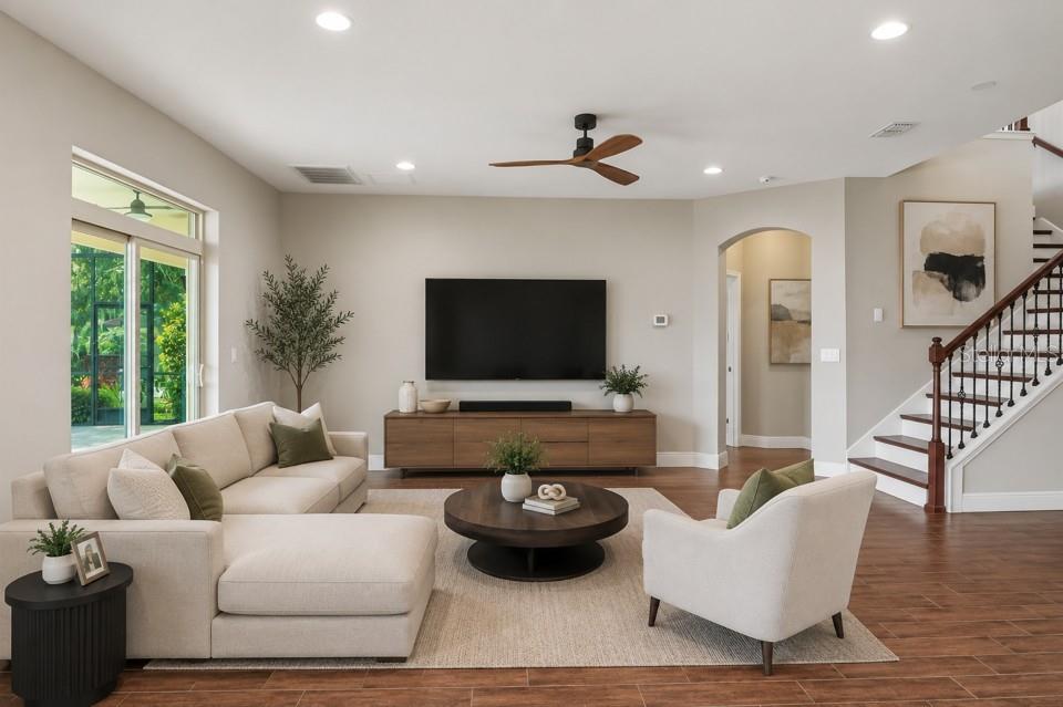 A living room features a sectional sofa, round coffee table, television, and a wooden staircase — 19711 WELLINGTON MANOR BOULEVARD, LUTZ, FL