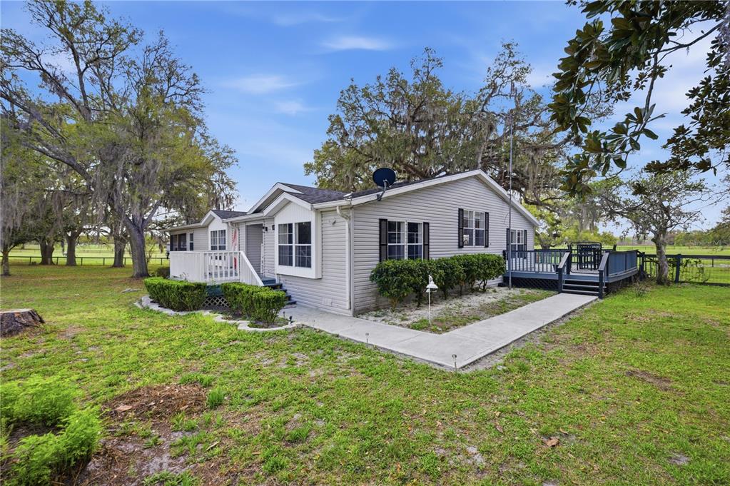 A light-gray, single-story house with a deck and a concrete walkway in a grassy yard — 18850 SE 12TH LANE, WILLISTON, FL