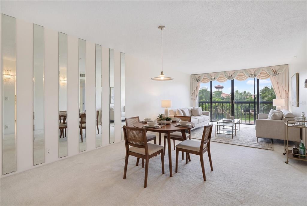 A dining area with vertical wall mirrors and a living room overlooking a balcony view — 255 DOLPHIN POINT UNIT 307, CLEARWATER BEACH, FL