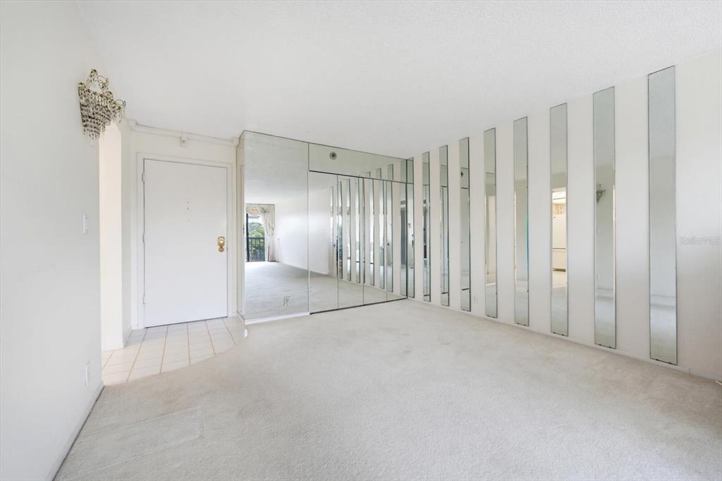 A living room features white carpeting, a mirrored wall, and a tiled entryway — 255 DOLPHIN POINT UNIT 307, CLEARWATER BEACH, FL