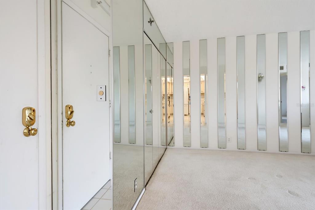 A room with beige carpeting, a white door, and walls featuring vertical mirror panels — 255 DOLPHIN POINT UNIT 307, CLEARWATER BEACH, FL