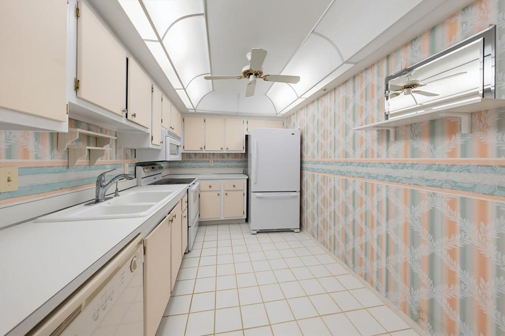 A galley kitchen features white appliances, light-colored cabinets, tiled flooring, and patterned wallpaper — 255 DOLPHIN POINT UNIT 307, CLEARWATER BEACH, FL