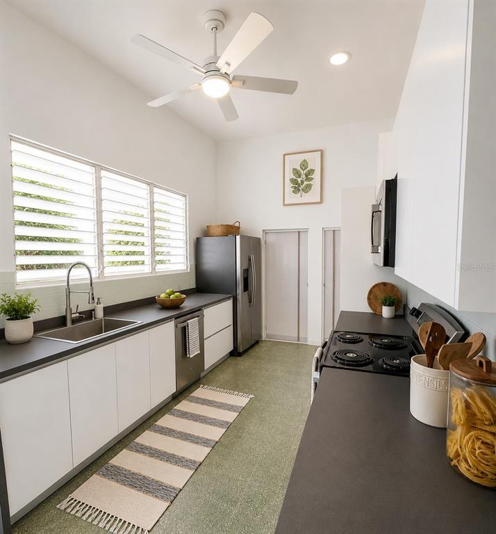 A modern galley kitchen features white cabinets, dark countertops, stainless steel appliances, and green flooring — F-6 CALLE GENOVA UNIT F-6, GUAYNABO, PR